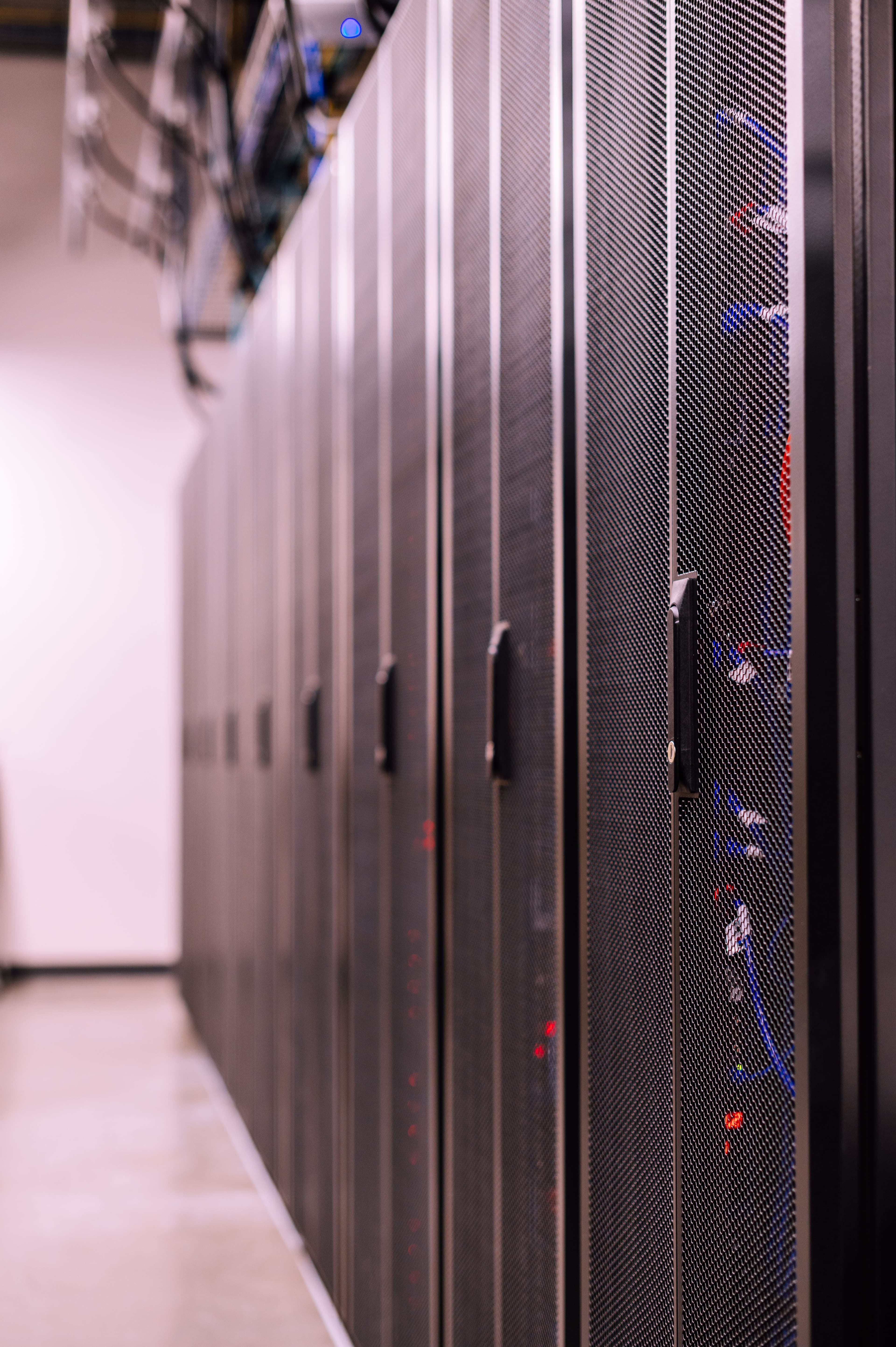 A corridor of black server racks with fiber patch cables