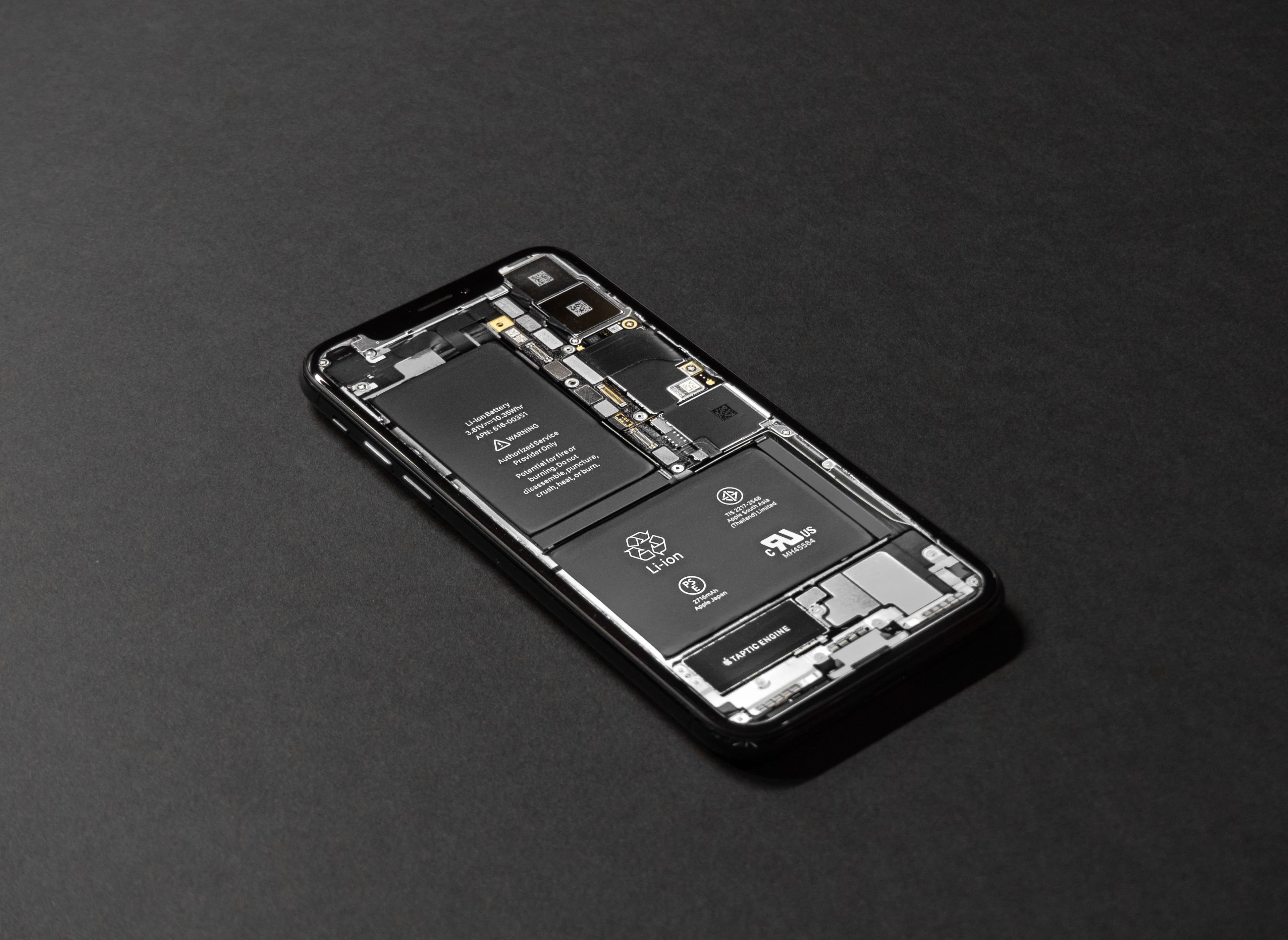 A disassembled smartphone with internal circuitry exposed on a dark surface